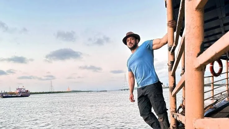 Indian actor posing on a riverside boat deck wearing a blue shirt and hat