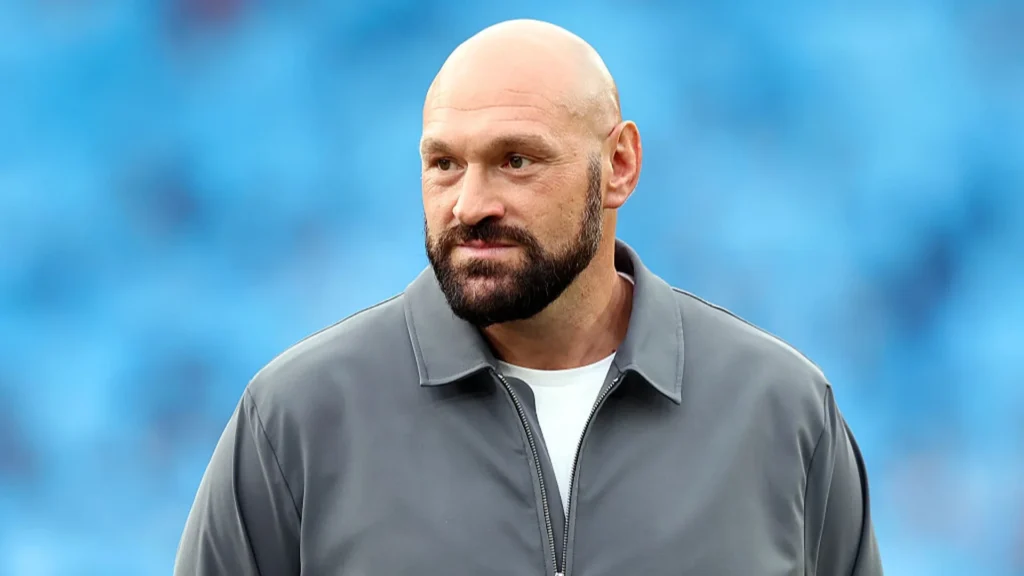 Tyson Fury wearing a gray jacket against a blue background