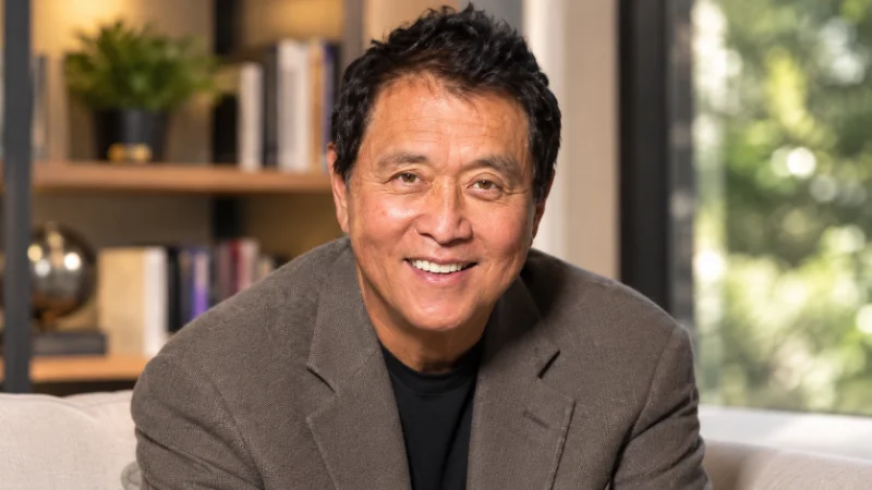 Robert Kiyosaki net worth wealth-building desk with books, coins, and a house model
